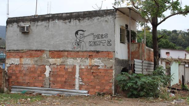 Auf einer Hauswand ist ein Graffiti mit der Aufschrift „PRES MENTE“ zu sehen.