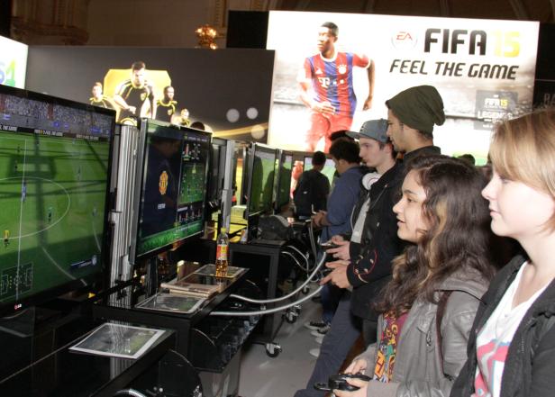 Eine Gruppe von Leuten spielt das Videospiel FIFA 15 auf mehreren Bildschirmen.