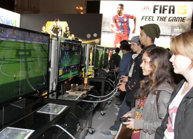 Eine Gruppe von Jugendlichen spielt das Videospiel FIFA 15 an mehreren Bildschirmen.