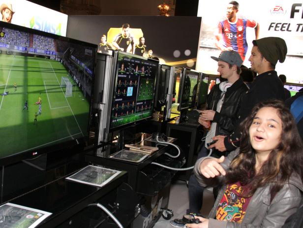 Mehrere Personen spielen an Spielstationen das Videospiel FIFA.