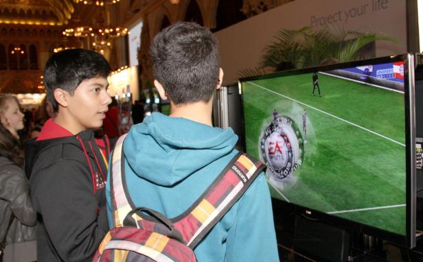 Zwei Jugendliche schauen einem Fußballspiel auf einem großen Bildschirm zu.