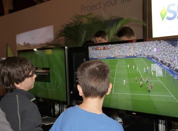 Zwei Jungen spielen ein Fußballvideospiel auf großen Bildschirmen.