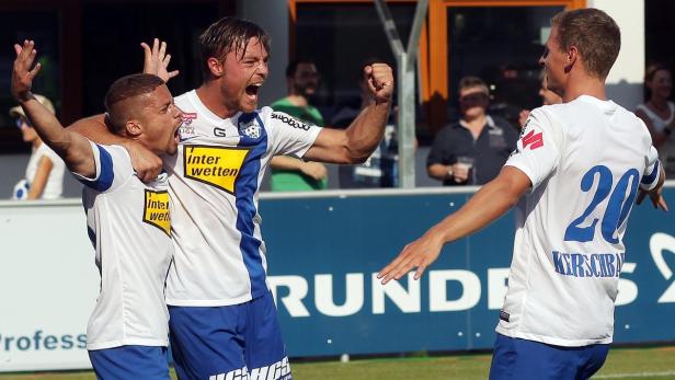 Drei Fußballspieler in weißen und blauen Trikots jubeln über einen Sieg.