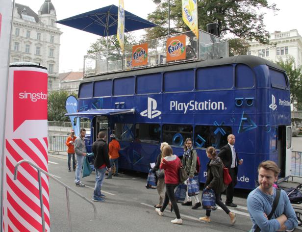 Ein blauer Doppeldeckerbus mit PlayStation- und Fanta-Werbung zieht Passanten an.