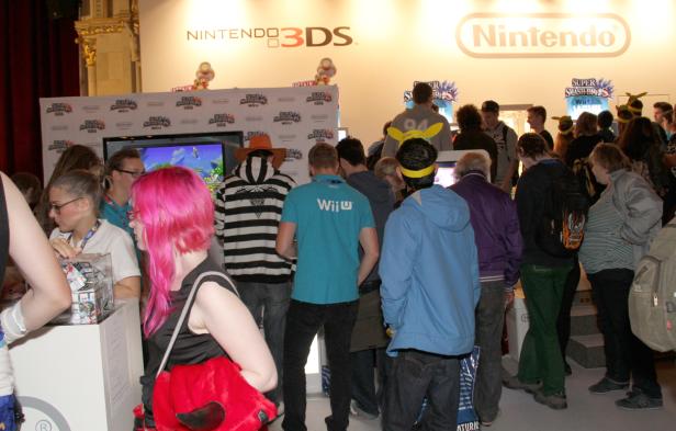 Viele Menschen stehen an einem Stand von Nintendo und spielen Videospiele.