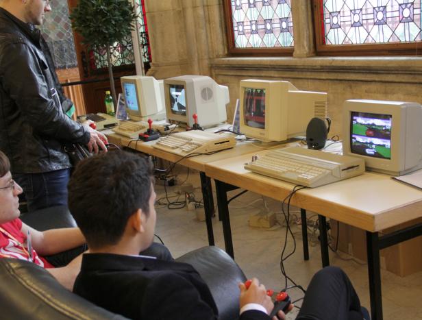 Mehrere Personen spielen an einer Reihe von Commodore-Computern mit Joysticks.
