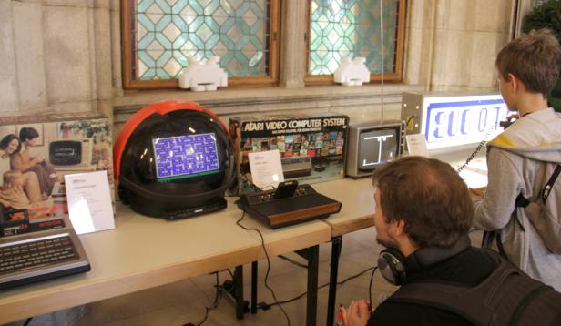 Auf einem Tisch stehen verschiedene Retro-Spielkonsolen, darunter ein Atari-System und ein Vectrex-Automat.