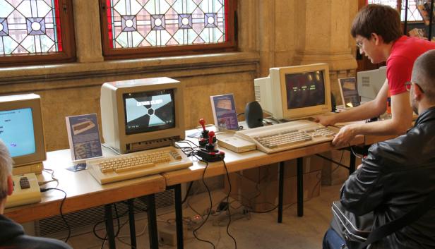 Auf einem Tisch stehen mehrere Commodore-Computer mit Monitoren und Joysticks.