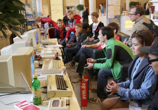 Eine Gruppe von Menschen spielt Computerspiele an alten Commodore-Computern mit Joysticks.