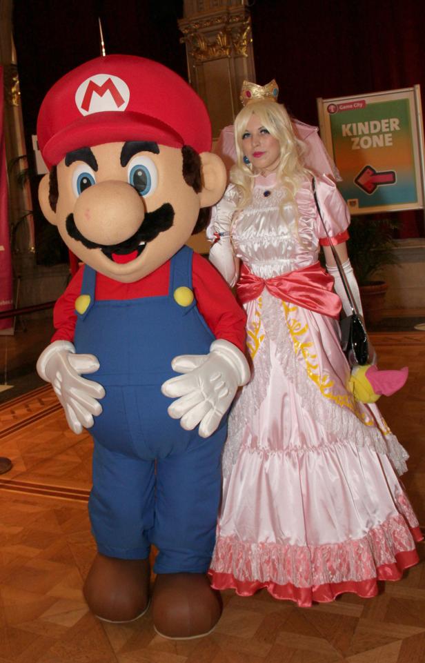 Ein Mario-Maskottchen und eine als Prinzessin Peach verkleidete Frau posieren für ein Foto.