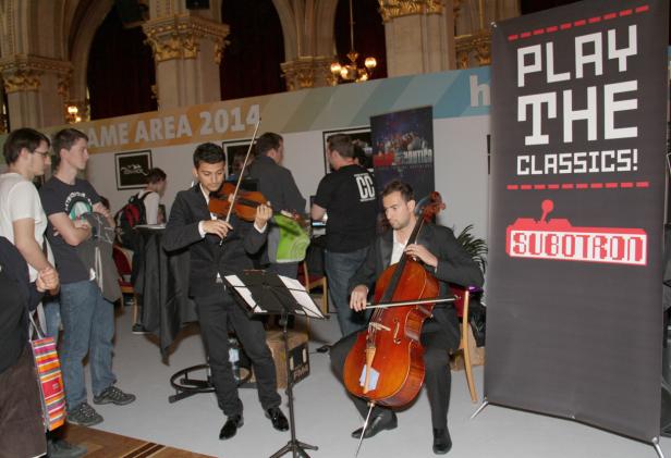 Ein Duo spielt Violine und Cello vor einem „Play the Classics“-Banner auf einer Veranstaltung.