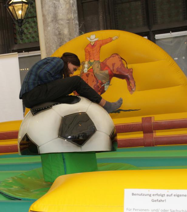 Eine Person reitet auf einem Hüpfball in Form eines Fußballs vor einer Hüpfburg mit Cowboy-Motiv.