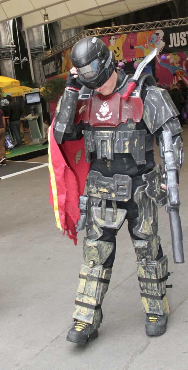 Eine Person in einem aufwendigen, handgefertigten Cosplay-Kostüm mit Helm und Waffe.