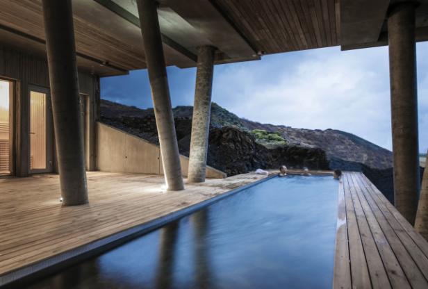 Menschen entspannen sich in einem Außenpool mit Blick auf eine vulkanische Landschaft.