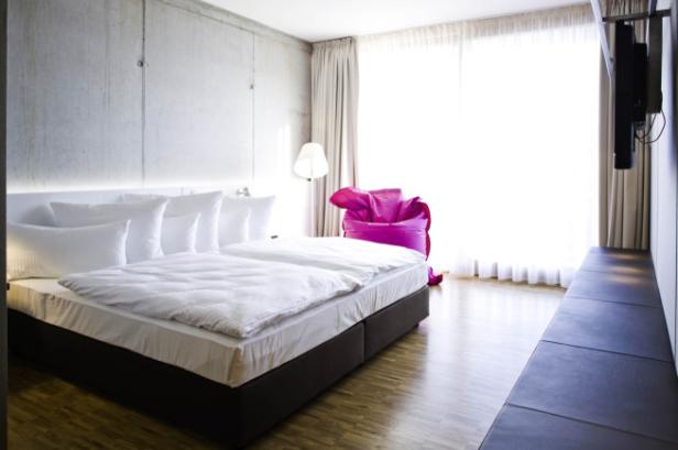 Ein modernes Schlafzimmer mit Doppelbett, Betonwand und einem pinkfarbenen Sitzsack.