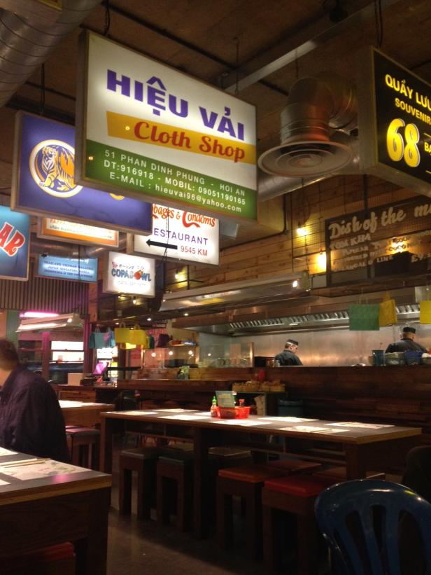 Innenansicht eines asiatischen Restaurants mit verschiedenen Schildern und Köchen bei der Arbeit.