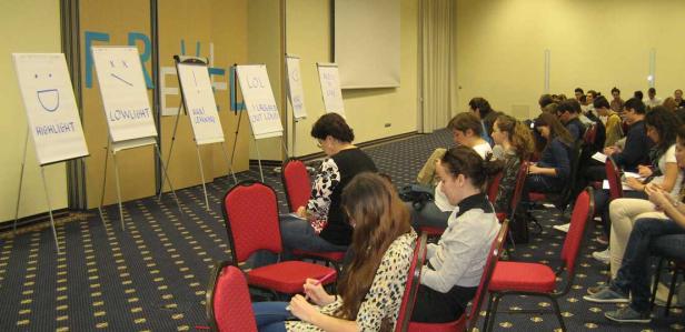 Zuschauer sitzen in einem Raum vor Flipcharts mit Aufschriften wie „Highlight“ und „LOL“.