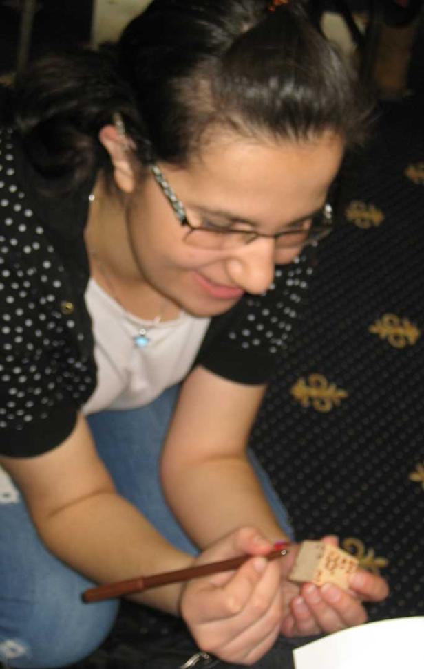 Eine Frau mit Brille bemalt einen kleinen Holzstempel mit einem Pinsel.