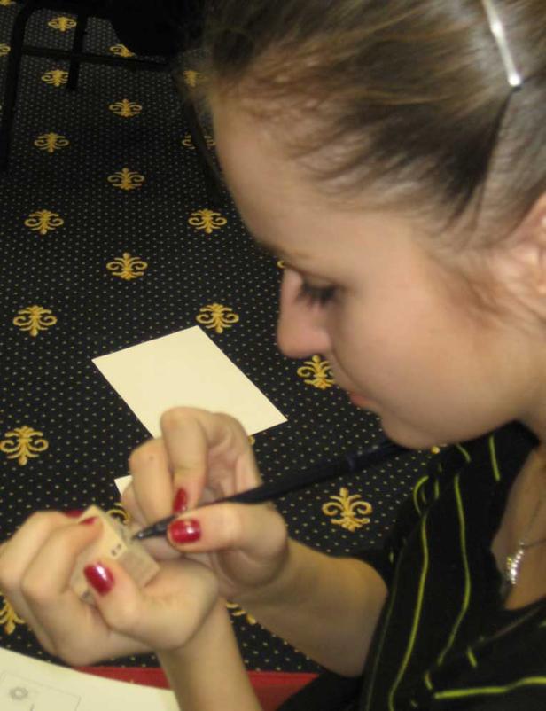 Eine Frau bemalt einen kleinen Holzstempel mit einem Pinsel.