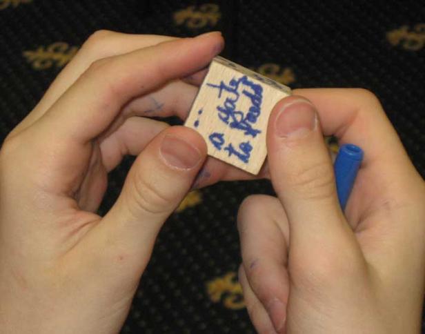 Zwei Hände halten einen Holzstempel mit blauer Schrift.