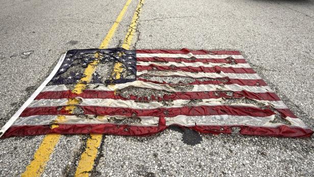 Eine beschädigte amerikanische Flagge liegt auf einer asphaltierten Straße.
