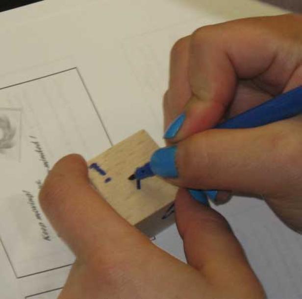 Eine Person bemalt einen Holzklotz mit einem blauen Stift.