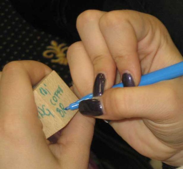 Eine Person beschriftet einen Holzklotz mit einem blauen Stift.