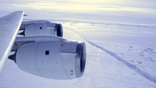 Blick aus dem Flugzeugfenster auf eine schneebedeckte Landschaft mit Gletscherspalten.