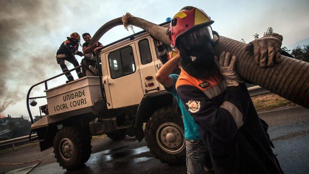 Feuerwehrleute halten einen Schlauch neben einem Löschfahrzeug der „Unidade Local Covas“.