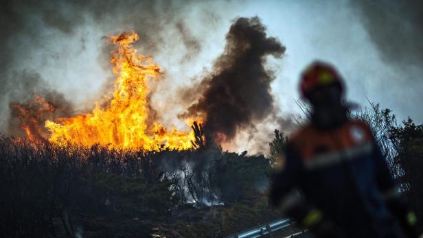 Ein Waldbrand wütet, während ein Feuerwehrmann im Vordergrund steht.