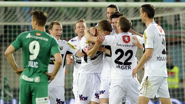 Fußballspieler umarmen sich auf dem Spielfeld, während ein Gegenspieler daneben steht.