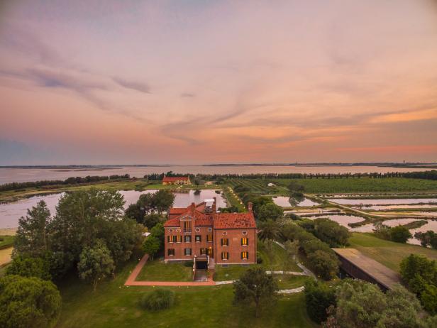 Ein großes Backsteingebäude auf einer grünen Wiese am Wasser bei Sonnenuntergang.
