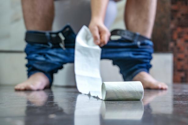 Mann auf der Toilette, ihm rollt das WC-Papier davon.