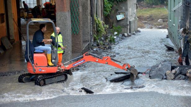 Ein Bagger räumt Geröll und Schlamm von einer überfluteten Straße.