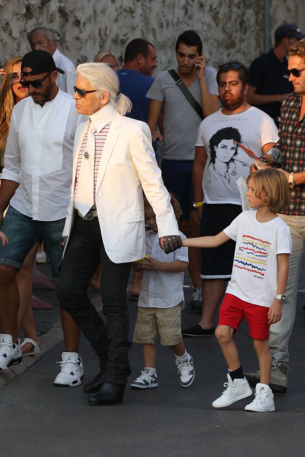 Karl Lagerfeld mit zwei Kindern, eines davon hält seine Hand.