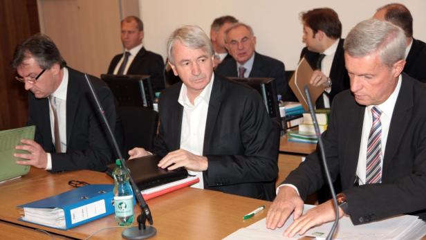 Mehrere Männer in Anzügen sitzen an einem Tisch bei einer Konferenz oder Sitzung.