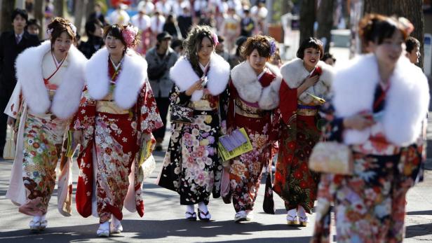 Eine Gruppe junger Frauen in Kimonos und mit Fellkragen geht die Straße entlang.