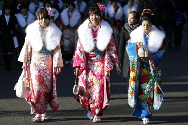 Drei junge Frauen in Kimonos mit Fellkragen nehmen an einer traditionellen japanischen Zeremonie teil.