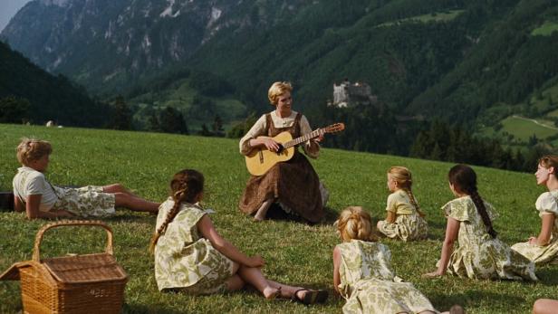 Maria singt mit den Kindern der Familie Trapp auf einer grünen Wiese mit Blick auf die Berge.
