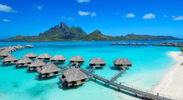 Bungalows mit Strohdächern ragen aus dem türkisfarbenen Wasser einer tropischen Insel.