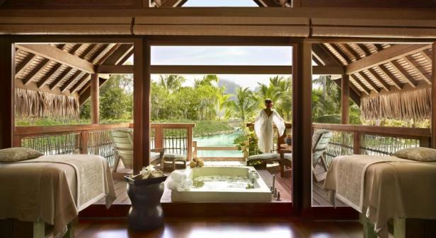 Ein Spa-Bereich mit Massageliegen und einer Badewanne im Freien mit Blick auf tropische Vegetation.