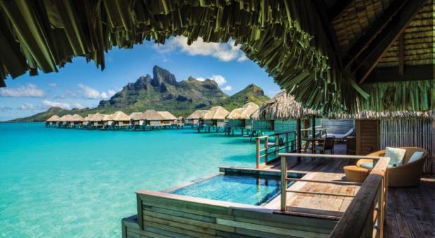 Bungalows auf dem Wasser vor einer tropischen Bergkulisse.
