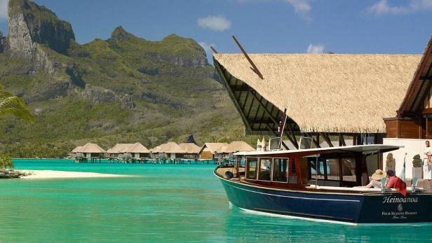 Ein Boot liegt vor einem Luxusresort mit strohgedeckten Bungalows auf dem Wasser.