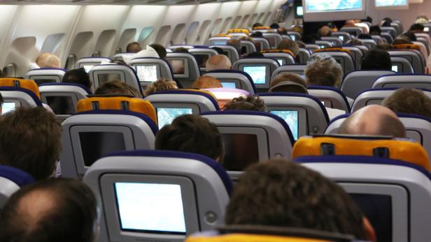 Passagiere sitzen in einem Flugzeug und schauen auf die Bildschirme vor ihnen.