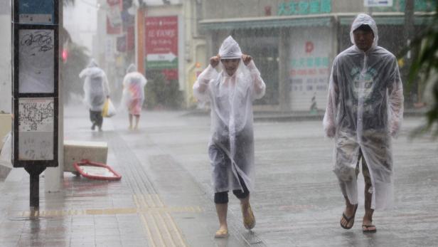 Menschen gehen in durchsichtigen Regenmänteln durch den strömenden Regen.