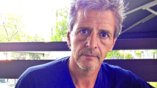 Ein Mann mit grauen Haaren und blauem T-Shirt blickt in die Kamera.