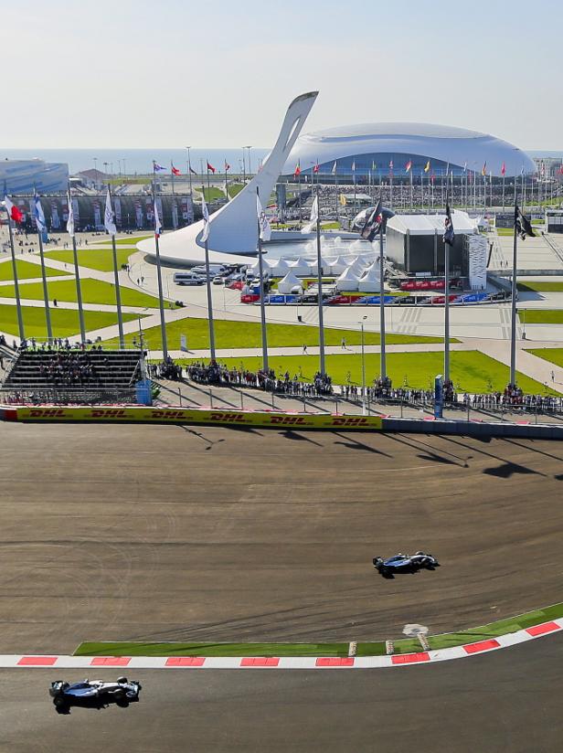 Zwei Formel-1-Autos rasen auf dem Sotschi-Autodrom, im Hintergrund das Olympiagelände.