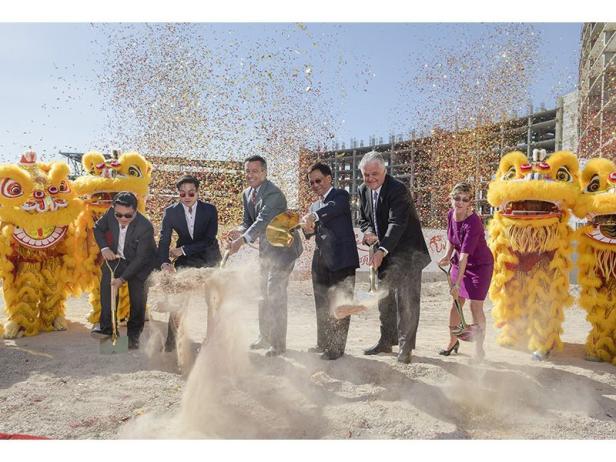 Mehrere Personen nehmen an einer Spatenstichzeremonie teil, umgeben von Löwentänzern und Konfetti.