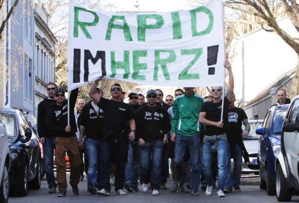 Eine Gruppe von Rapid Wien Fans demonstriert mit einem Transparent auf der Straße.