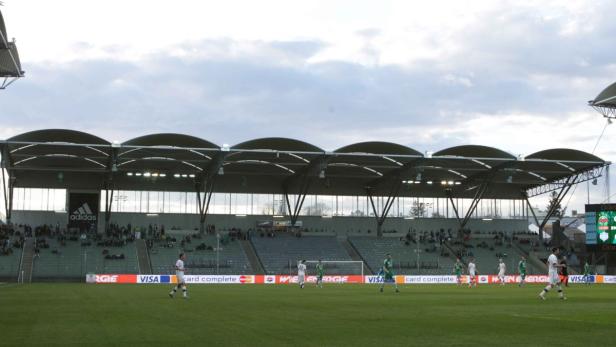 Ein Fußballspiel in einem Stadion mit Zuschauern und einer großen Adidas-Werbung.